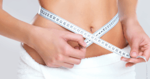 Person measuring waistline to track sustainable weight loss progress while following a Semaglutide or Tirzepatide treatment plan. How to Build a Sustainable Workout Routine While on Semaglutide or Tirzepatide